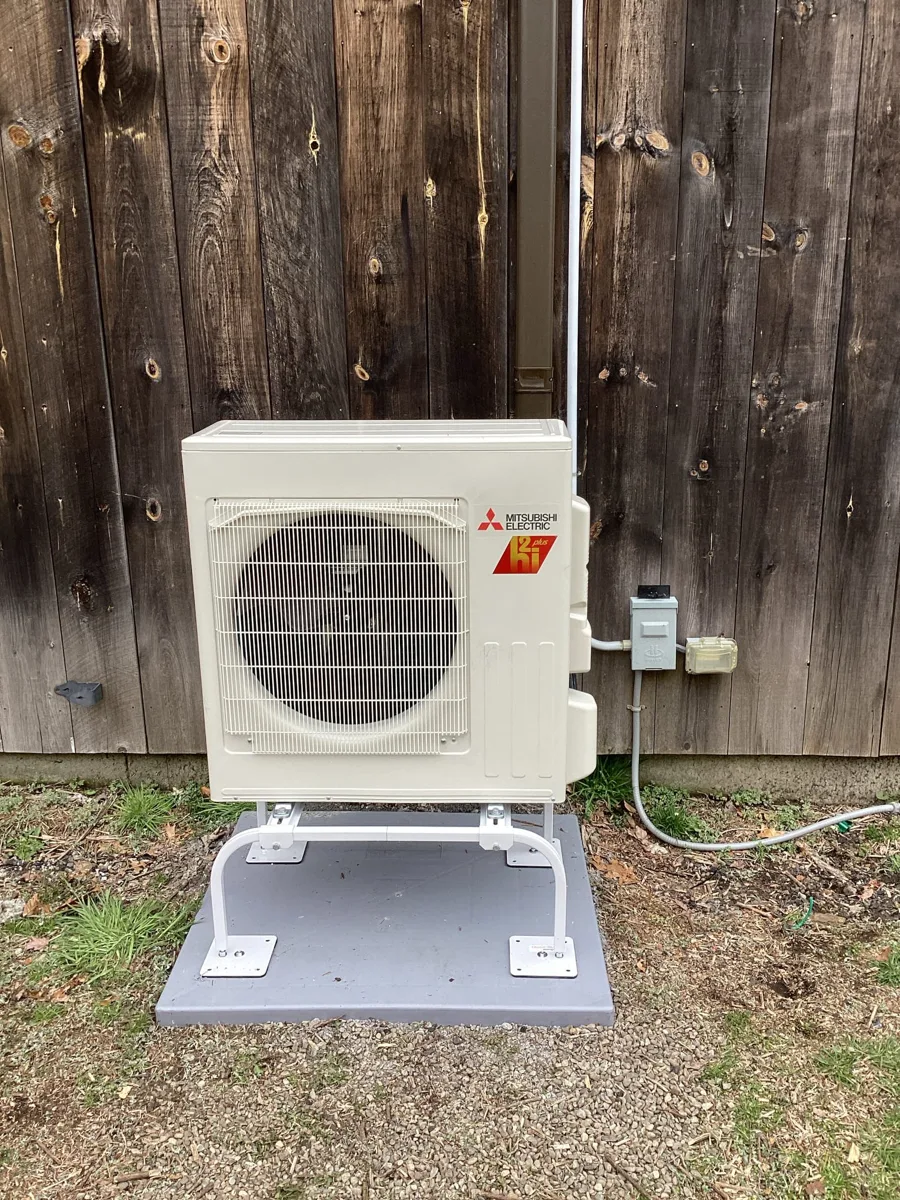 Mitsubishi mini-split outdoor unit on a stand against a weathered wood barn wall in Easton, CT, installed by Celco